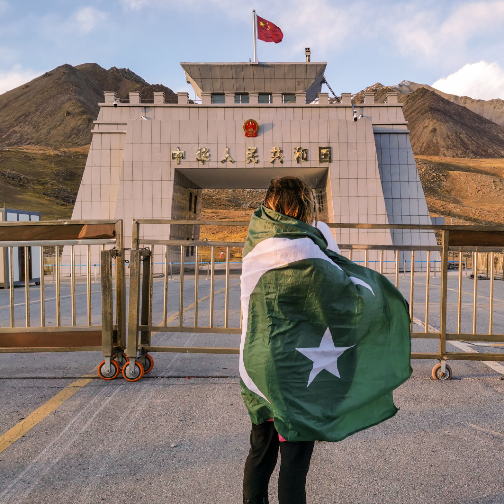 Warm Encounters At The Icy Border: Visiting Khunjerab Pass From Hunza Valley 15 Girl wrapped in Pakistani flag in front of the Pakistan-China border at Khunjerab Pass.