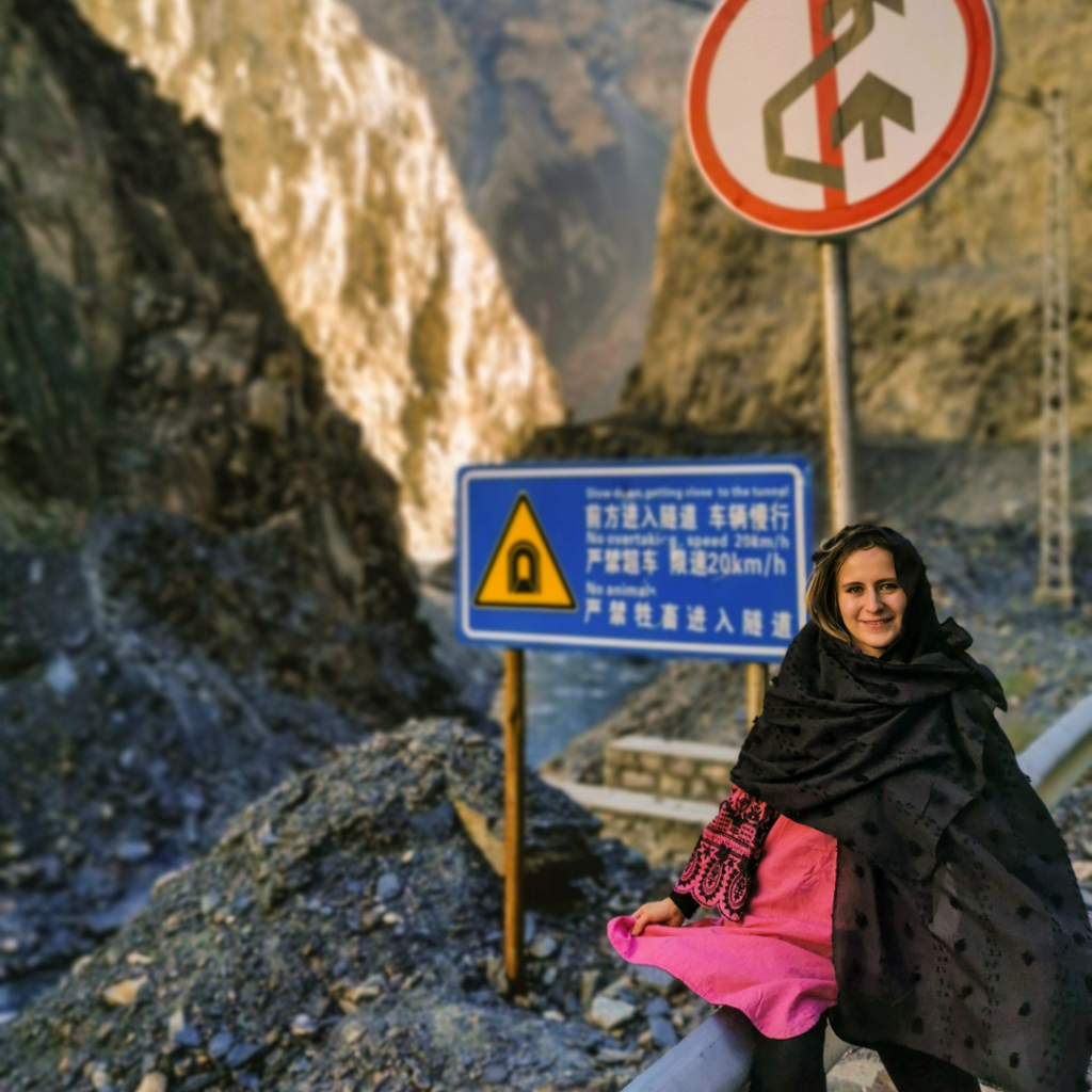 Warm Encounters At The Icy Border: Visiting Khunjerab Pass From Hunza Valley 9 Girl sitting in front of a Chinese language road sign near Khunjerab Pass, Pakistan.