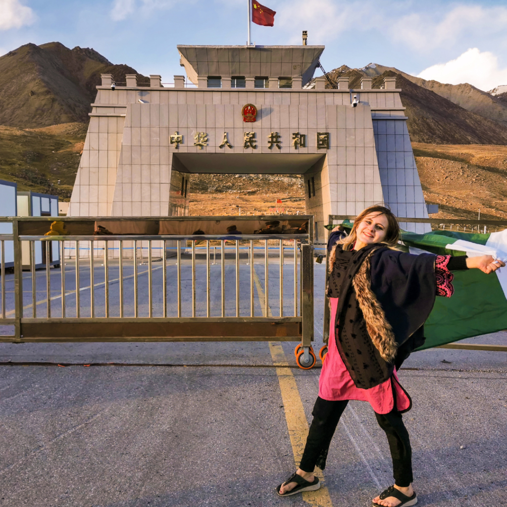 Warm Encounters At The Icy Border: Visiting Khunjerab Pass From Hunza Valley 10 Foreign girl with Pakistani flag posing in front of the Pakistan-China border at Khunjerab Pass.