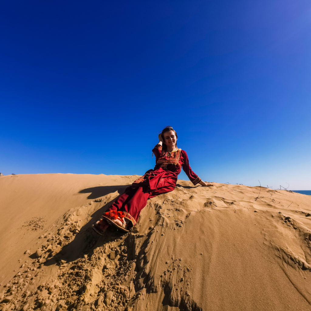 Full Itinerary For An Incredible Balochistan Day Trip From Karachi 8 Foreign girl in traditional Balochi dress sitting on a sand dune by the beach in Balochistan, Pakistan.