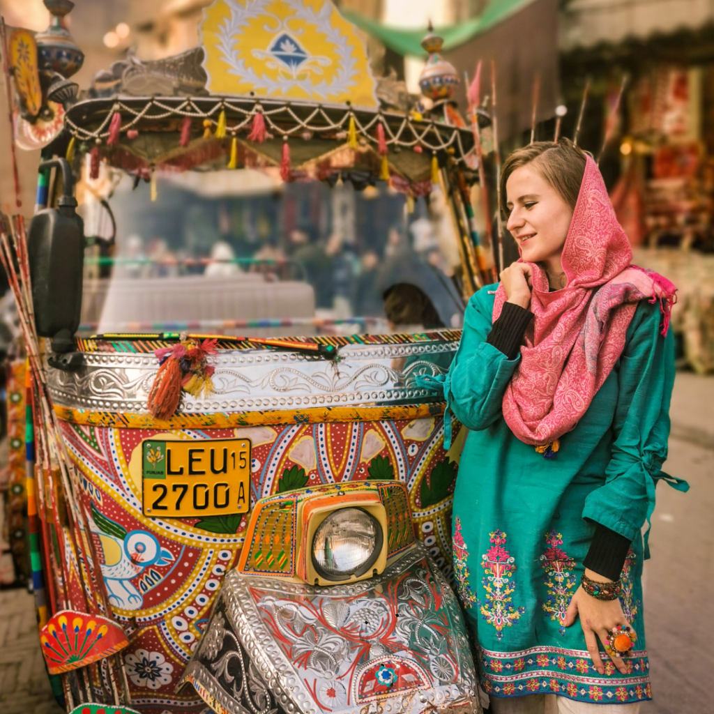 Foreign girl in traditional clothes next to a colorfully decorated rickshaw in the Walled City of Lahore, Pakistan.