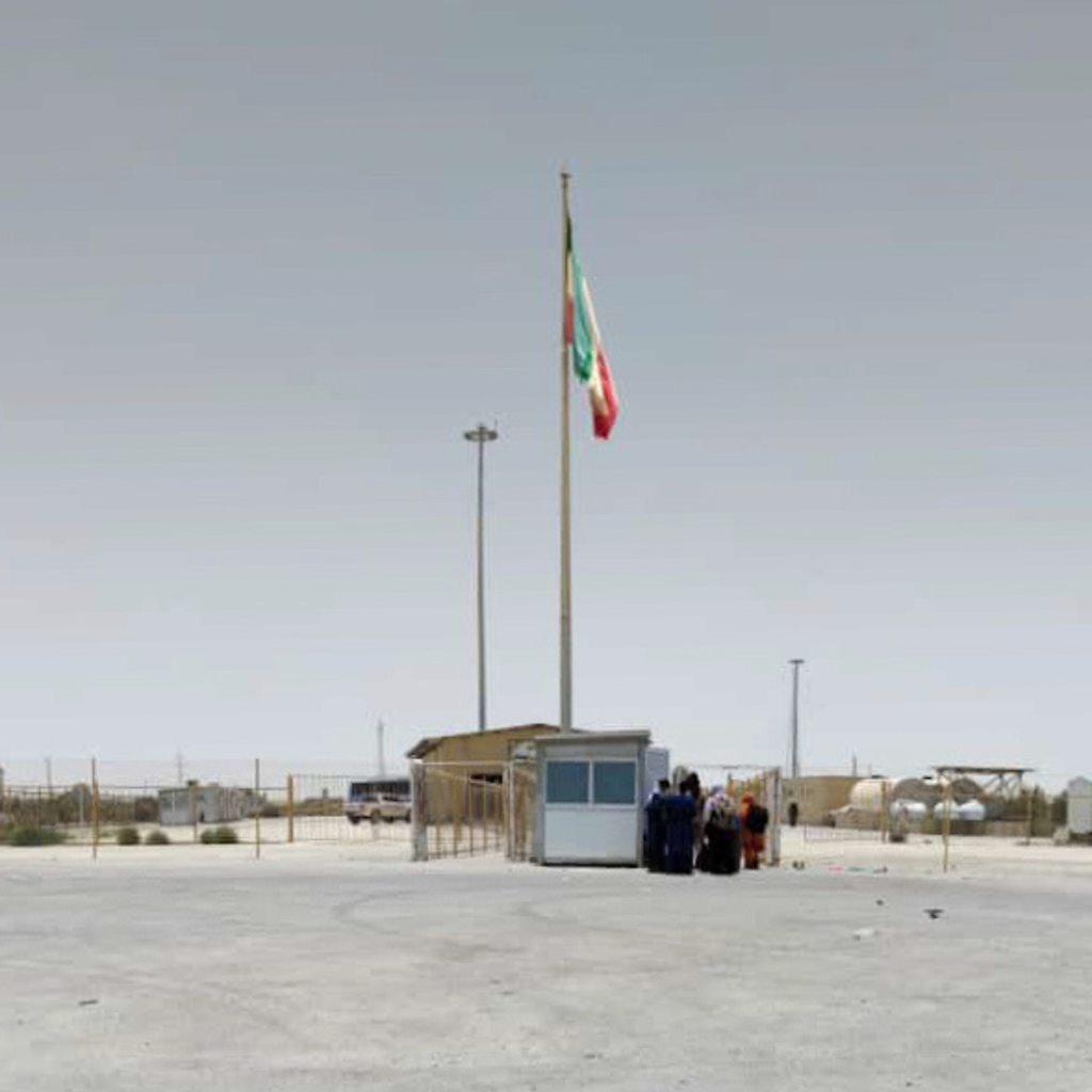 A group of travelers entering Iran from Pakistan via the Gabd Rimdan Border. A small white booth with a tall Iranian flag.
