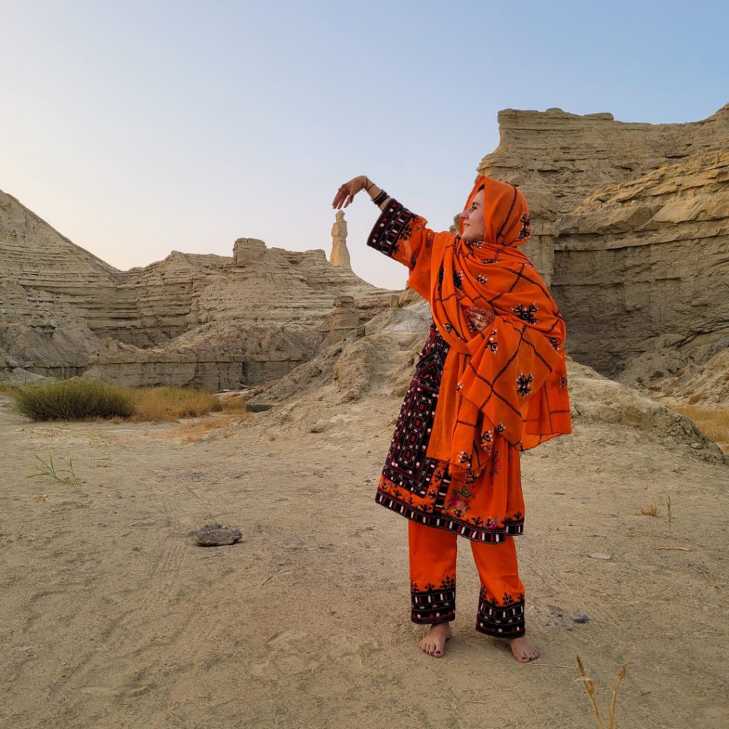Secret Balochistan - 10 Days Tour To One Of The LEAST VISITED PLACES ON EARTH 3 Tourist girl in orange Balochi dress striking a pose in front of the Princess of Hope structure in Hingol National Park, Balochistan, Pakistan